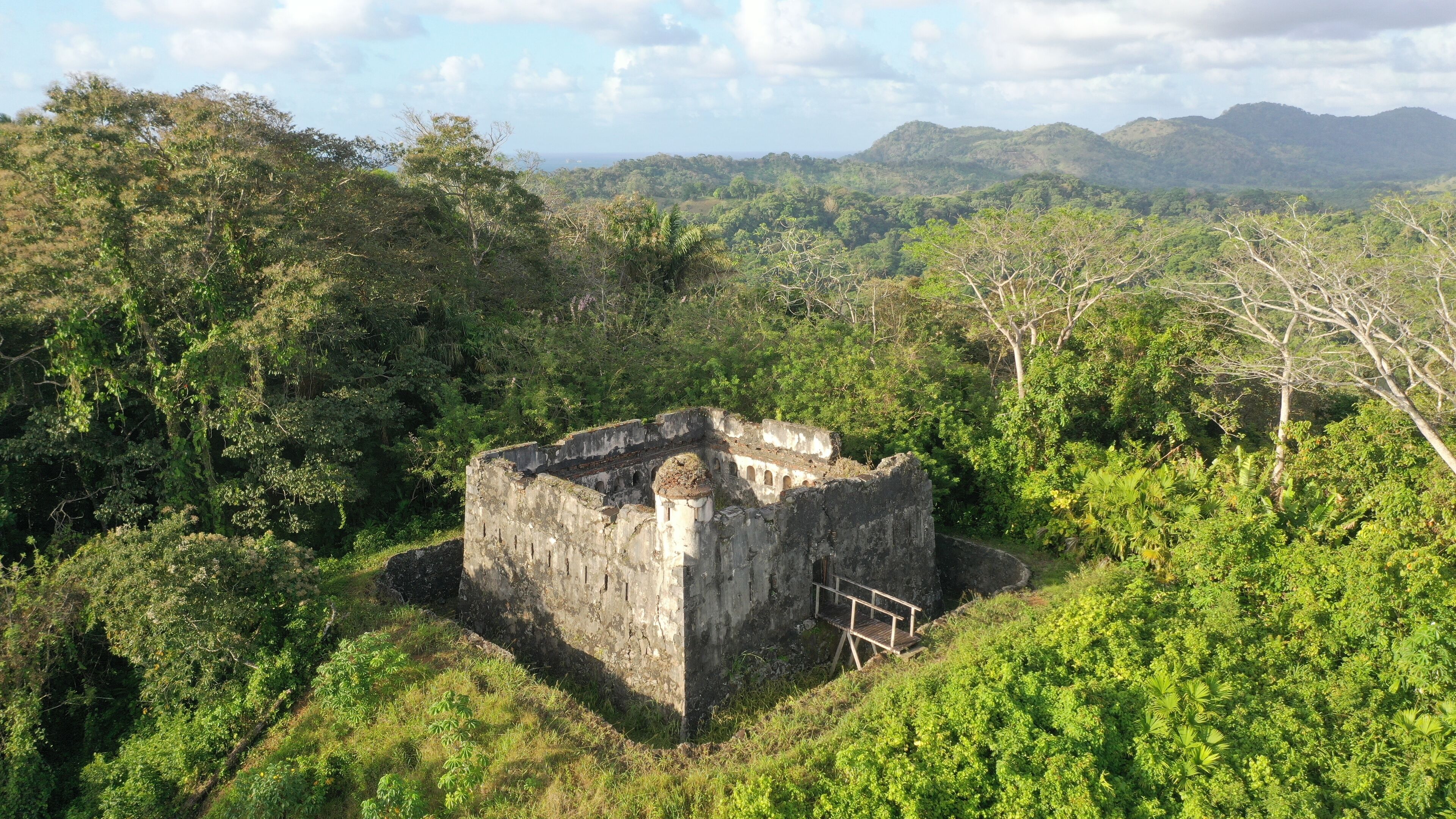 An ancient stone structure surrounded by dense forest and hills.
