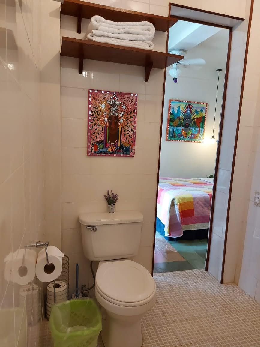 A bathroom with a toilet, a green trash bin, and a shelf with towels.