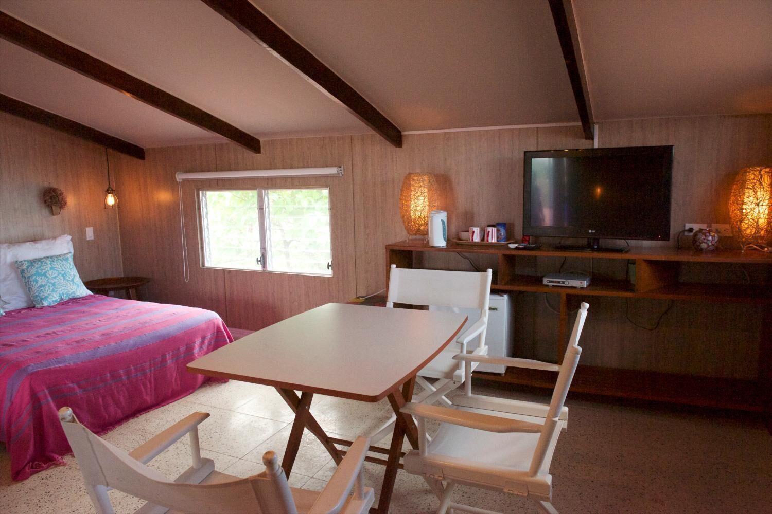 Quarto aconchegante com cama, mesa, cadeiras, televisão e escrivaninha com abajur.