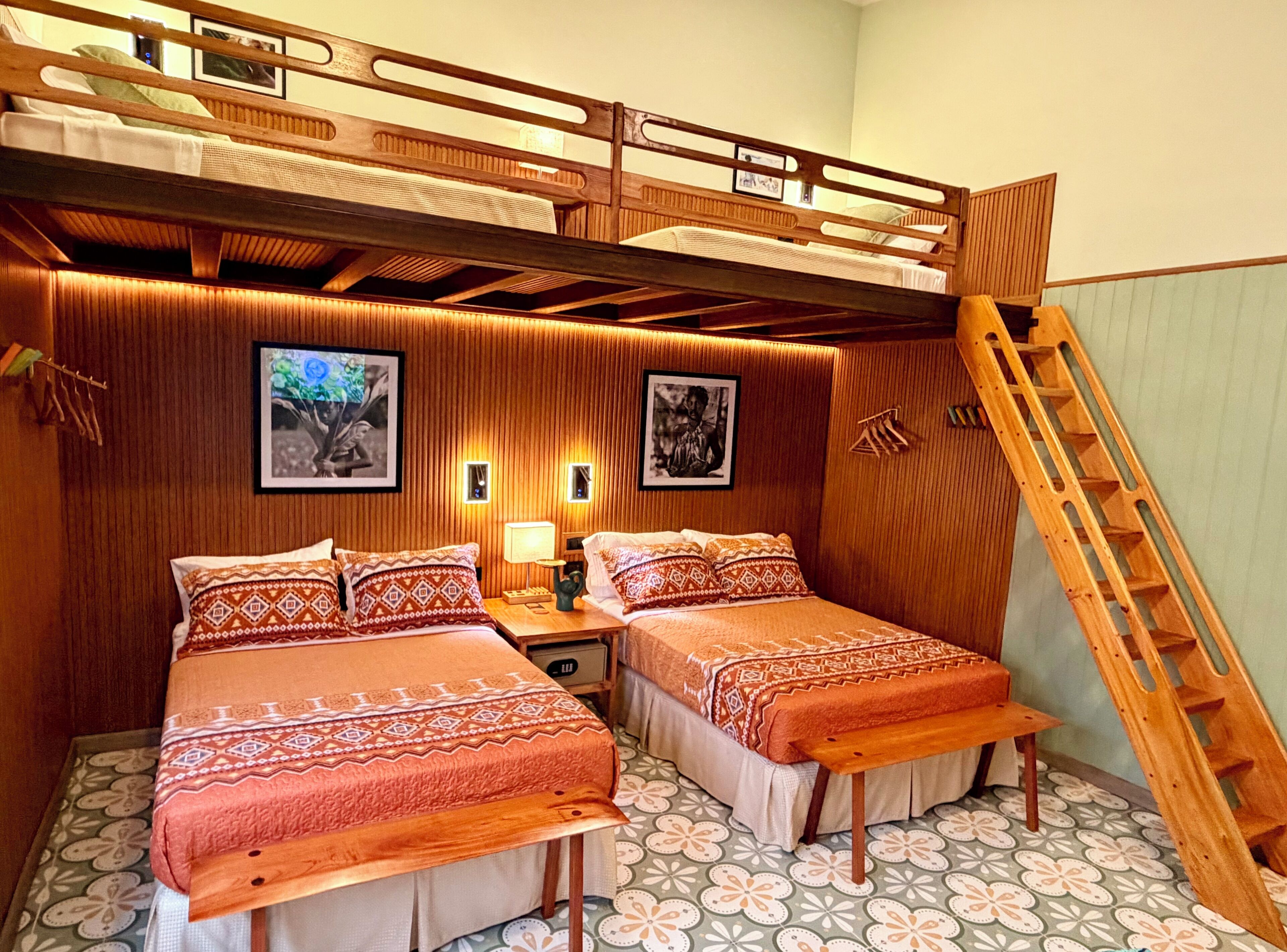 Una habitación con dos camas, una escalera de madera y una lámpara fijada a la pared.