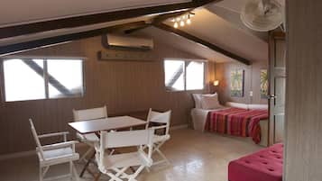 Una habitación acogedora con techo de madera, una mesa de comedor con sillas, una cama con manta colorida y un ventilador.