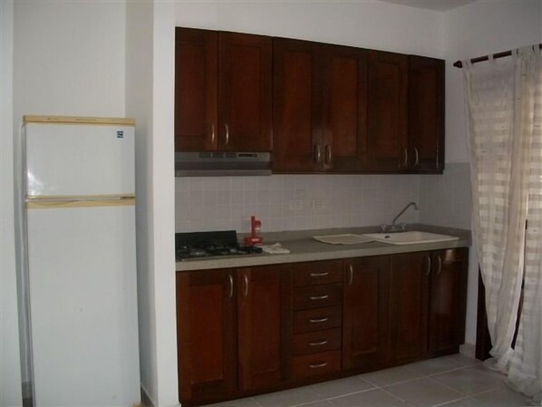 Una cocina con armarios de madera, un refrigerador blanco, un lavamanos y una ventana con cortina.