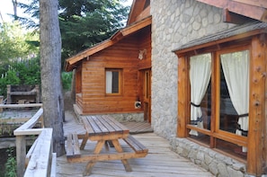 A wooden cabin with a stone exterior, a wooden deck, and a picnic table.
