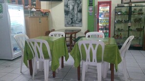A dining area with a table set for four, surrounded by white chairs, a refrigerator, and a Coca-Cola vending machine.