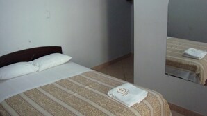 Un lit simple avec une couvre-lit à rayures et un oreiller blanc, un petit miroir accroché au mur et une serviette posée sur le lit.