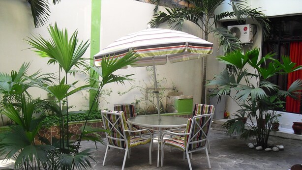 Une terrasse avec une table ronde et quatre chaises à rayures, entourée de plantes en pot et d’un parasol à rayures.