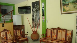 Un salon avec un canapé, deux fauteuils, un grand vase et un téléviseur fixé au mur.