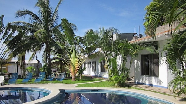 A swimming pool with tiled edges, surrounded by palm trees and lounge chairs. - Rivera del Mar (Puerto Escondido)