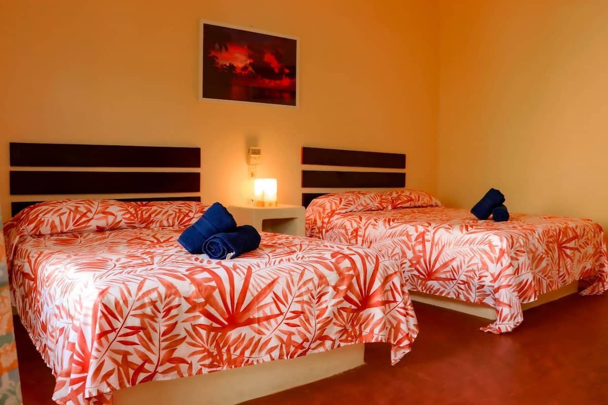 Habitación de hotel con dos camas, cada una con una colcha de hojas rojas y blancas y una toalla azul sobre una de ellas.