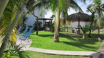 A garden with a thatched-roof structure, palm trees, and blue chairs.