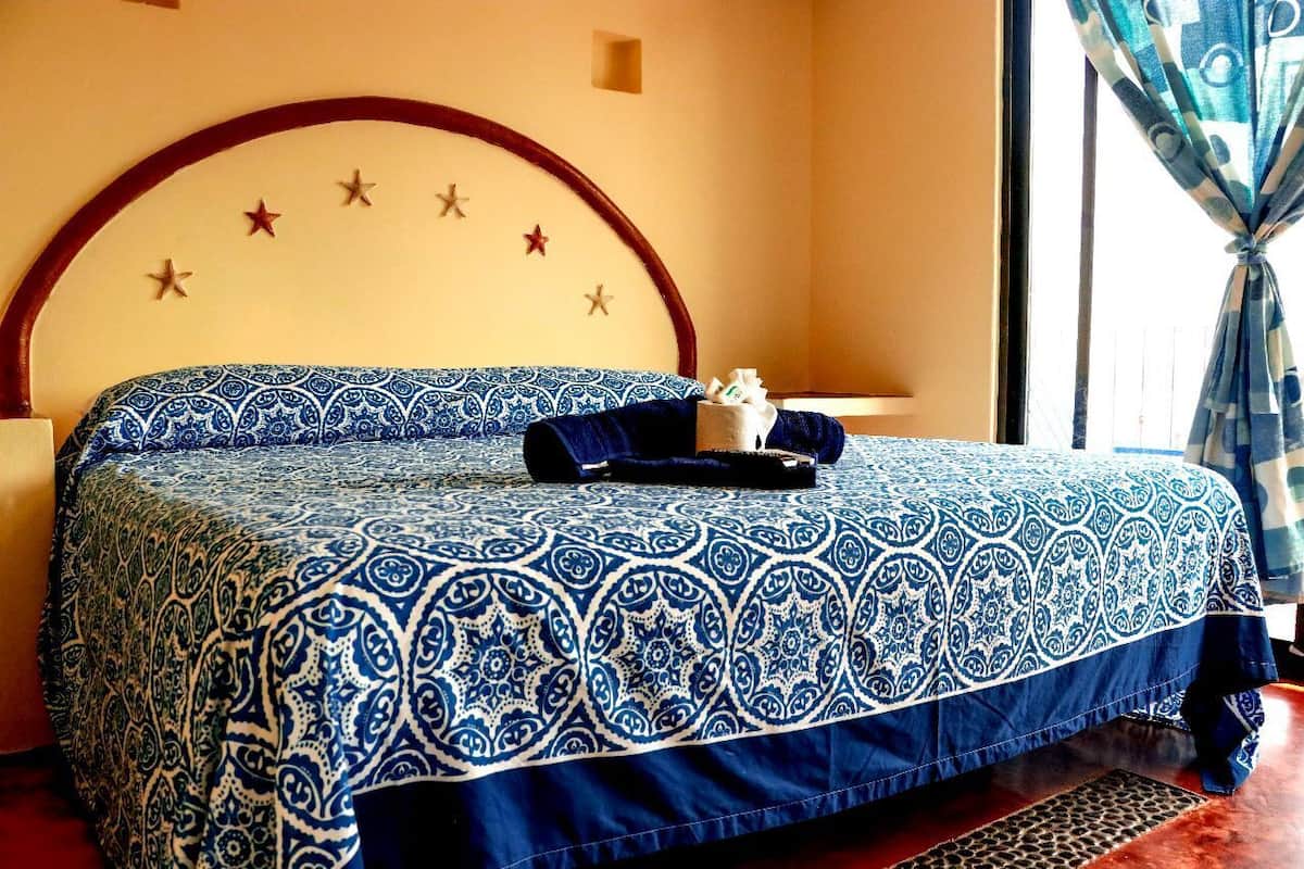 Una cama con una colcha azul y blanca estampada, un cabecero de madera con adornos de estrellas y una ventana con cortinas azules.