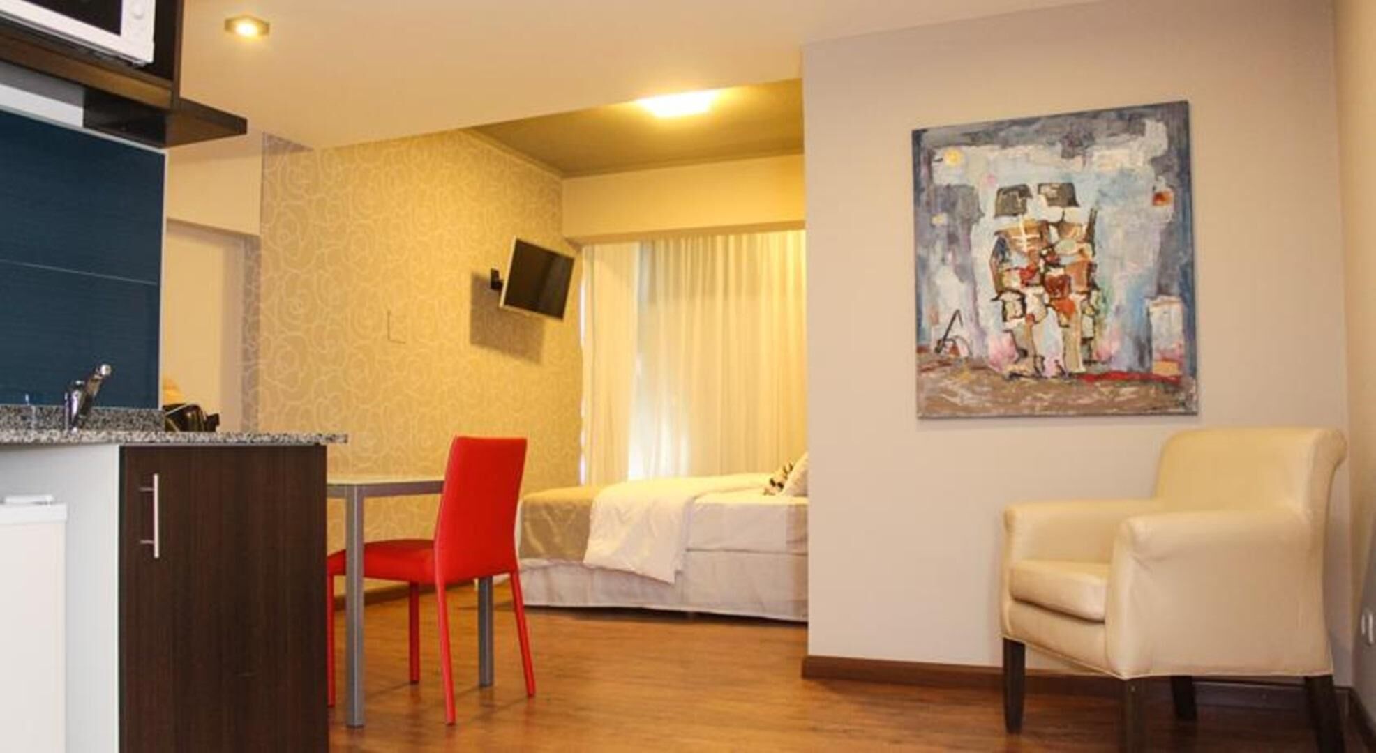 A compact hotel room with a bed, a desk with a chair, a television, and a painting on the wall.