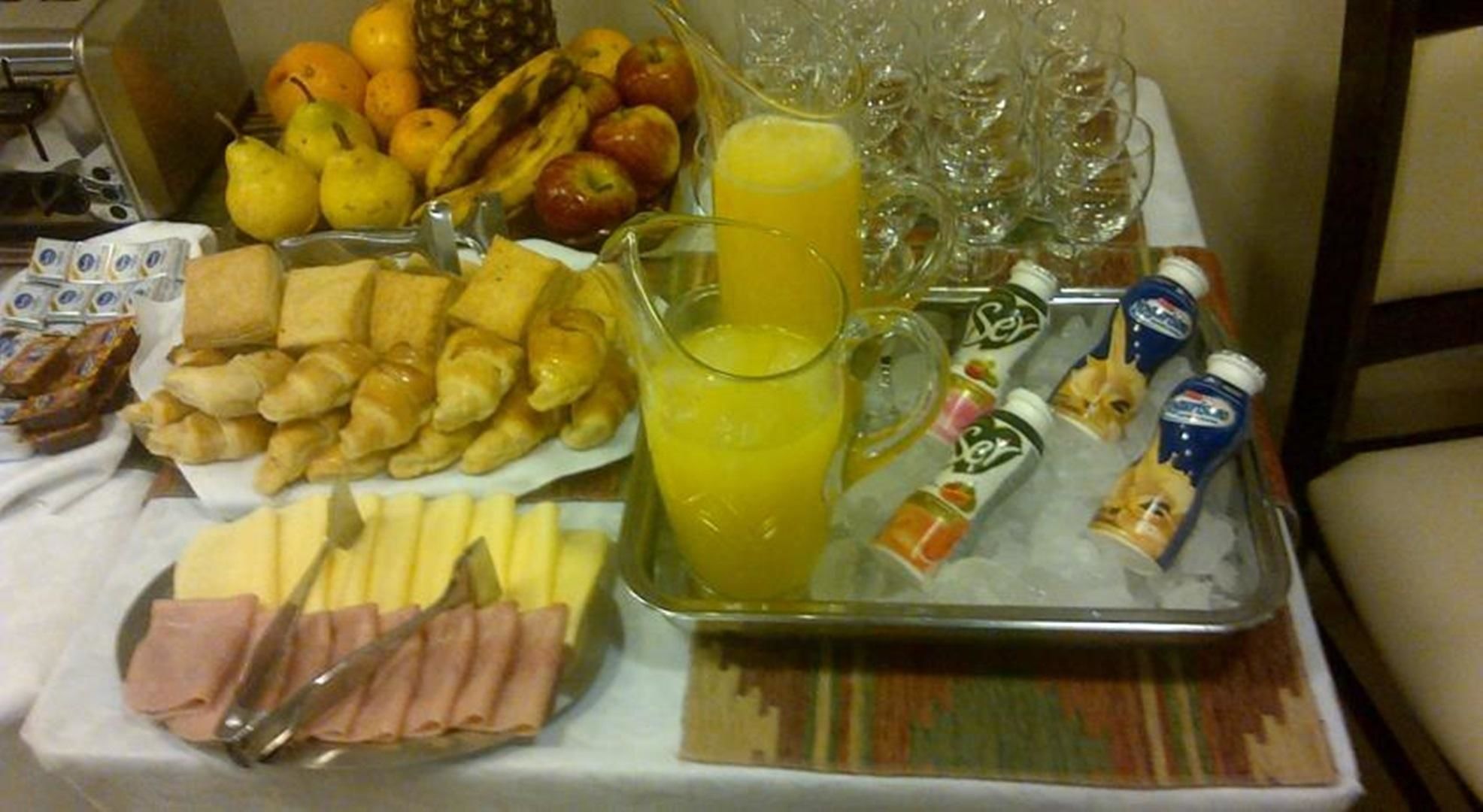 A breakfast buffet with various food items, a pitcher of orange juice, and several bottles of beverages.
