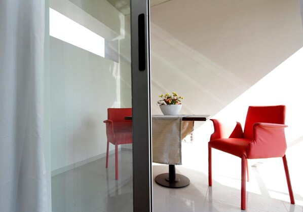 Un intérieur moderne avec une cloison en verre, une table ornée d’un vase de fleurs et deux chaises rouges.