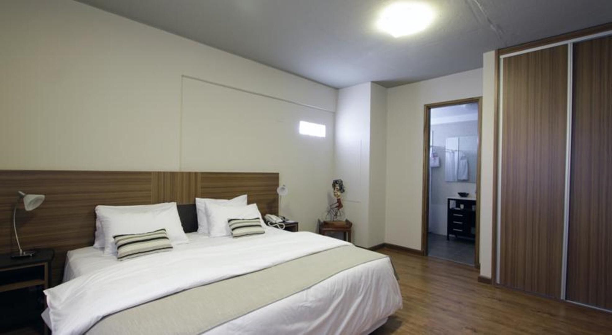 Ein Hotelzimmer mit einem großen Bett, einem Nachttisch mit Lampe, einem Kleiderschrank und einem durch eine offene Tür einsehbaren Badezimmer.