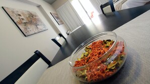 A dining table with a glass bowl containing dried herbs, a painting on the wall, and a bed in the background.