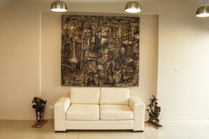 Un salón con un cuadro abstracto de gran tamaño en la pared, un sofá blanco y dos pequeñas esculturas en el suelo.