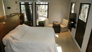 Een moderne slaapkamer met een groot bed, een bureau, een stoel, een televisie en een raam met uitzicht op bomen.