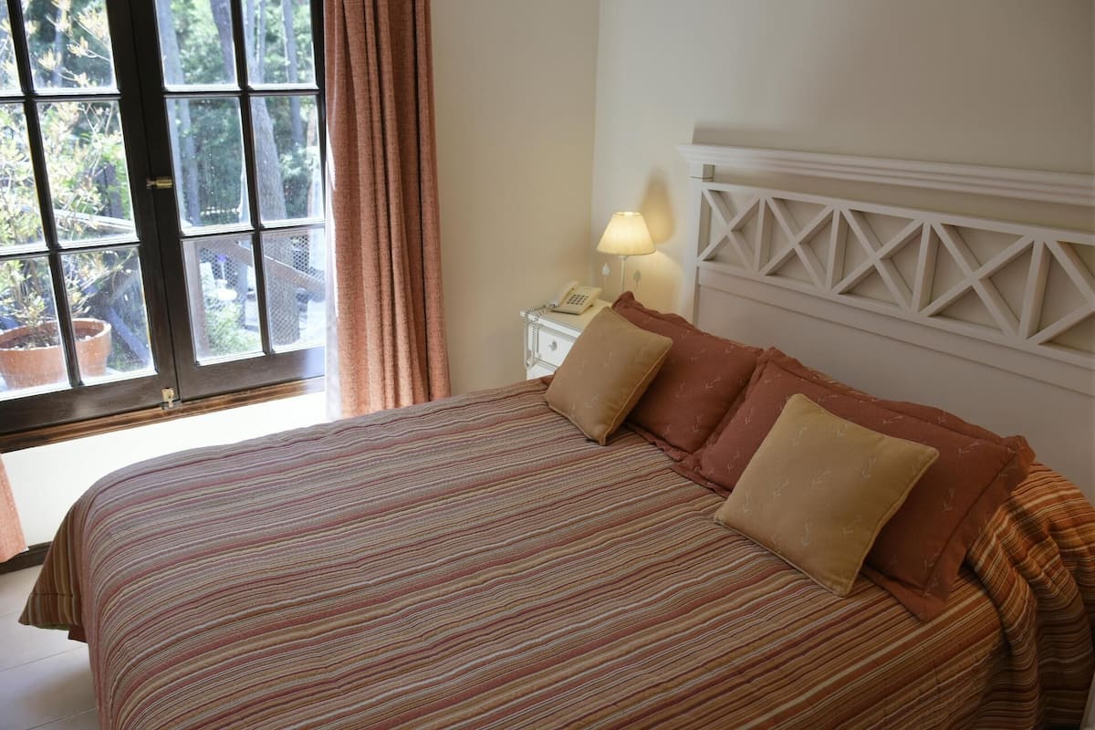 Uma cama com roupa de cama listrada, uma mesa de cabeceira com abajur e uma janela com cortinas.