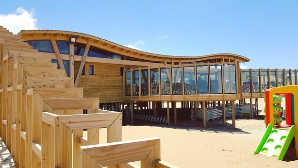 Une structure en bois dotée d’un toit incurvé et de grandes fenêtres, qui ressemble probablement à une maison de plage ou à un bâtiment d’un complexe hôtelier.