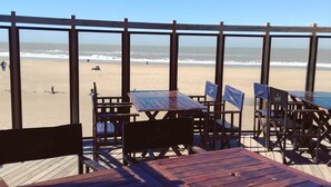 Une terrasse en bois avec des tables et des chaises donnant sur une plage.