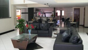 Una sala de estar moderna con una mesa de centro de vidrio, un sofá negro y un comedor al fondo.