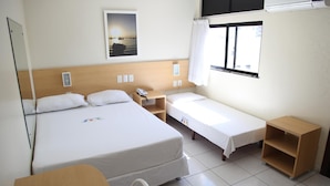 Habitación de hotel con una cama grande, una cama más pequeña, un escritorio, una silla, una ventana con cortinas y un aire acondicionado instalado en la pared.