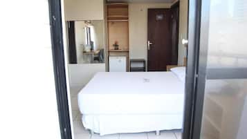 Quarto de hotel com cama, escrivaninha, cadeira, pequeno frigorífico e guarda-roupa.