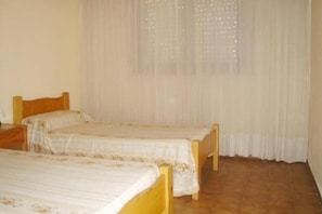 A room with two wooden beds, a window with sheer curtains, and a tiled floor.