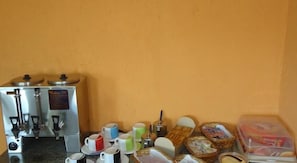 A kitchenette with a coffee maker, tea kettle, and a small refrigerator. There are cups, a jar, and a basket of bread on the counter. - Hotel Dueto (São Bernardo do Campo)
