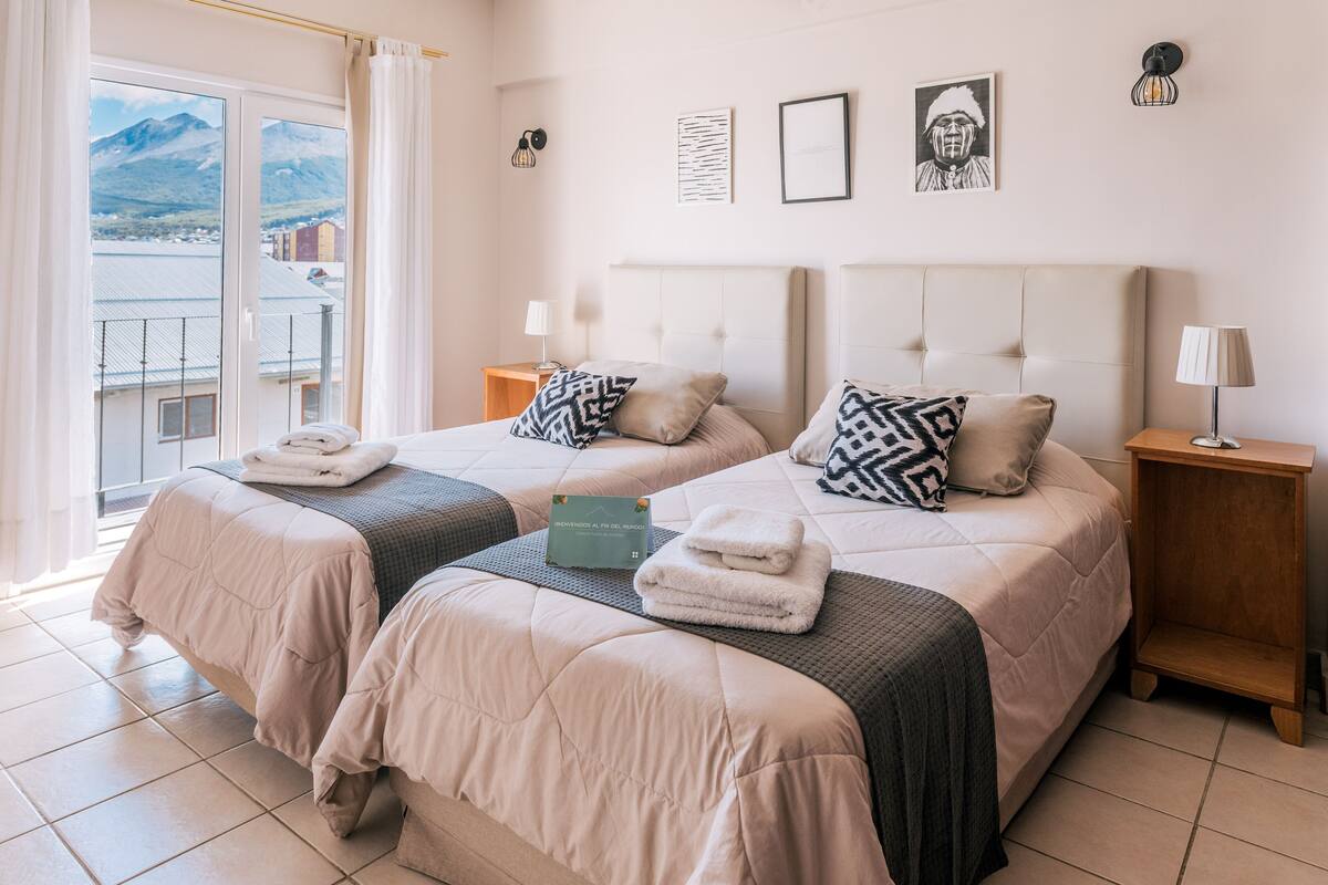 A hotel room with two beds, a balcony with a mountain view, and a sign indicating the room is for sale.