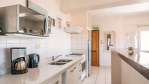 Ett modernt kök med vitvaror i rostfritt stål, vita köksluckor och en kakelbeklädd vägg bakom arbetsbänken.