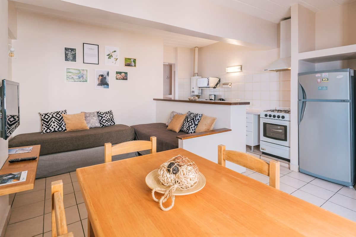 A modern kitchen with a built-in oven, a refrigerator, and a dining area with a wooden table and chairs.