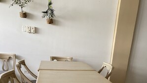 Une table à manger entourée de six chaises en bois, un plancher de couleur claire et un mur muni d’une prise électrique et orné de deux plantes en pot.