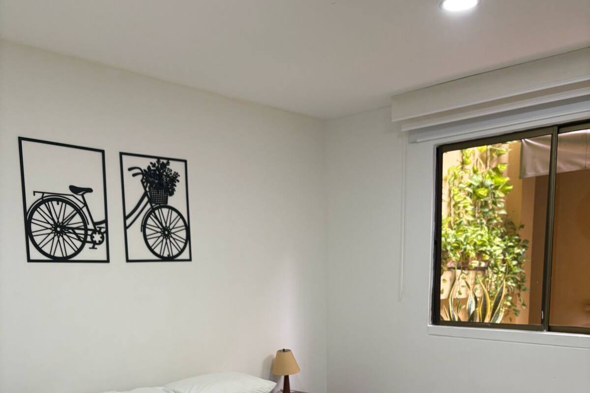 A bedroom with a bed, a nightstand, a lamp, and two wall art pieces.