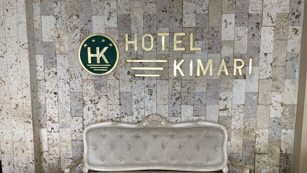 Un banc doté d’un dossier capitonné et de motifs décoratifs élaborés, placé devant un mur orné d’une mosaïque de carreaux de pierre et d’une enseigne indiquant « HÔTEL KIMARI ».