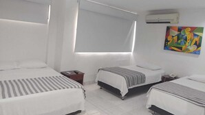 Une chambre d’hôtel avec deux lits simples, une fenêtre avec des rideaux, un appareil de climatisation et une peinture abstraite aux couleurs vives accrochée au mur.