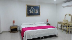 Une chambre à coucher comprenant un lit, un bureau, une chaise, une table de chevet, un climatiseur fixé au mur et un tableau encadré accroché au mur.