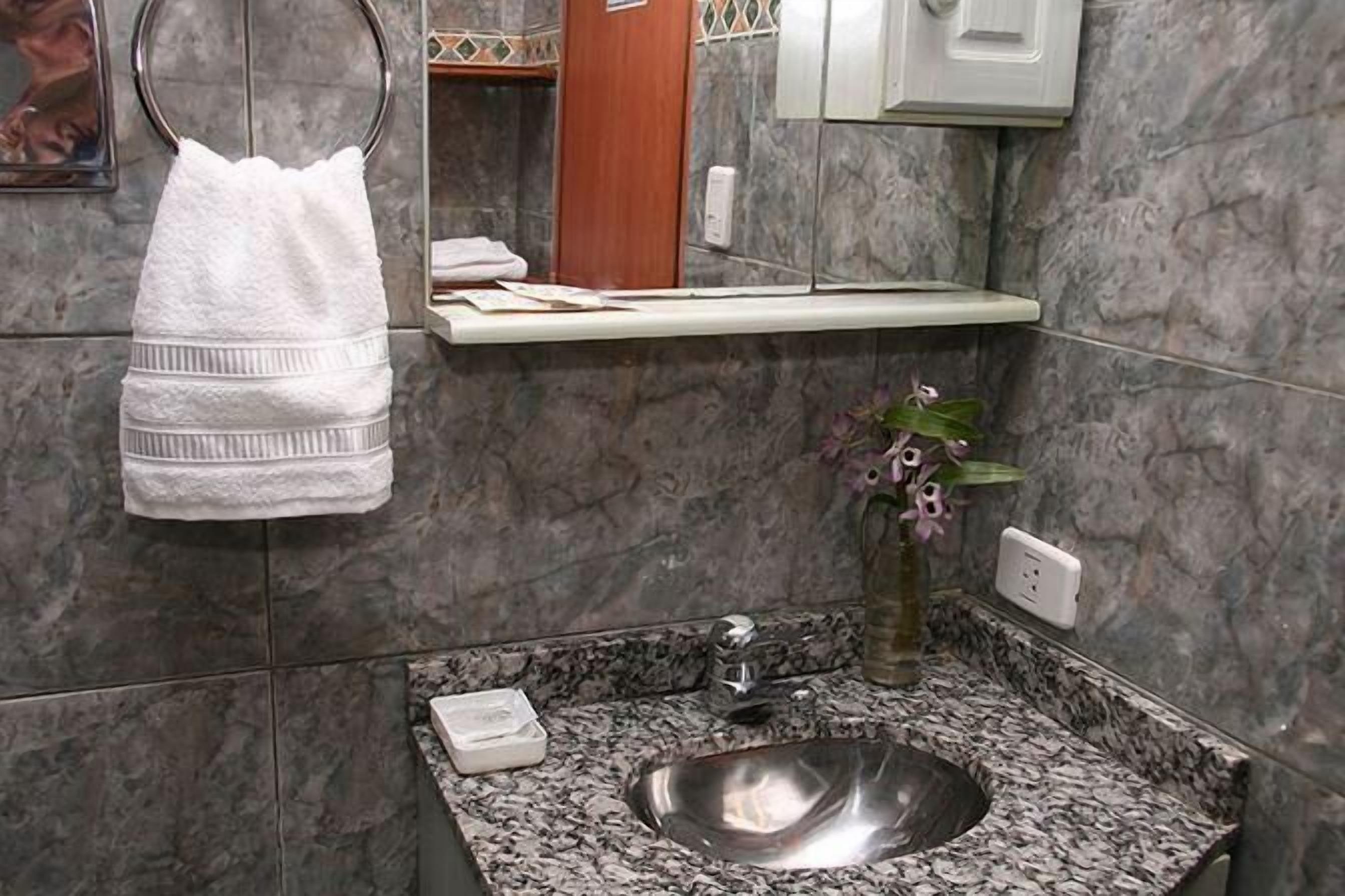 A bathroom with a marble sink, a towel hanging on a metal ring, a mirror, and a small plant.