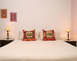 Una cama con dos almohadones decorativos, una mesita de noche con lámpara y dos cuadros en la pared.