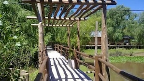A wooden bridge with a simple railing structure, surrounded by greenery and a body of water. - Amarran Sancho (Tigre)