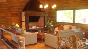A cozy cabin interior with a fireplace, wooden walls, a sofa, a dining table, and wicker chairs. - Amarran Sancho (Tigre)