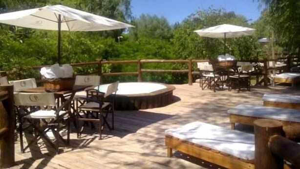 An outdoor patio area with wooden tables and chairs, white umbrellas, and a wooden deck. - Amarran Sancho (Tigre)