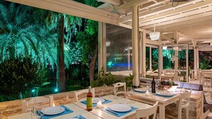 Un restaurant amb taules preparades per dinar, vistes a un jardí i una paret de pedra.
