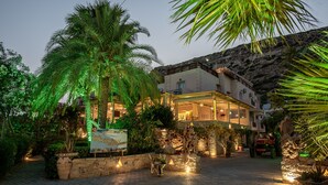 Un hotel amb un pati empedrat, palmeres i una paret de pedra.