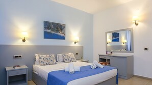 Habitació d'hotel amb un llit, taules de nit, un tocador amb mirall i llums penjades a la paret.