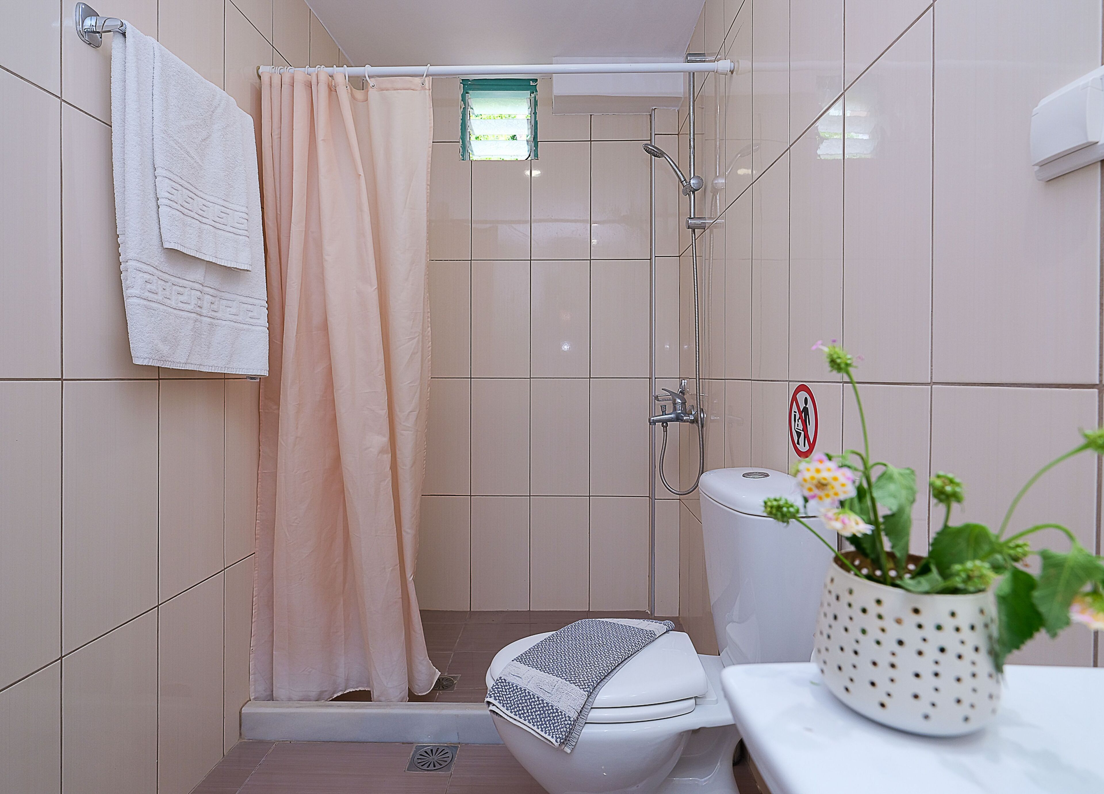 A bathroom with a shower, toilet, and a sink with a flower vase.