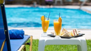 Taula al costat de la piscina amb dues begudes i un entrepà.