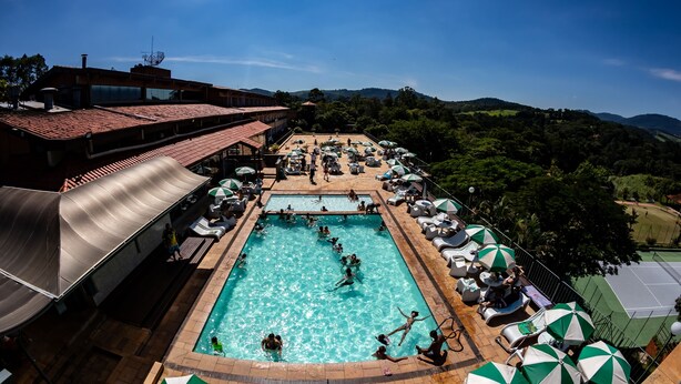 Una piscina en la azotea con agua cristalina, rodeada de sillones de descanso y sombrillas, con vistas a colinas y un cielo despejado.