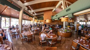 Un restaurante espacioso con techos altos, vigas de madera y una isla central con comida y bebidas.